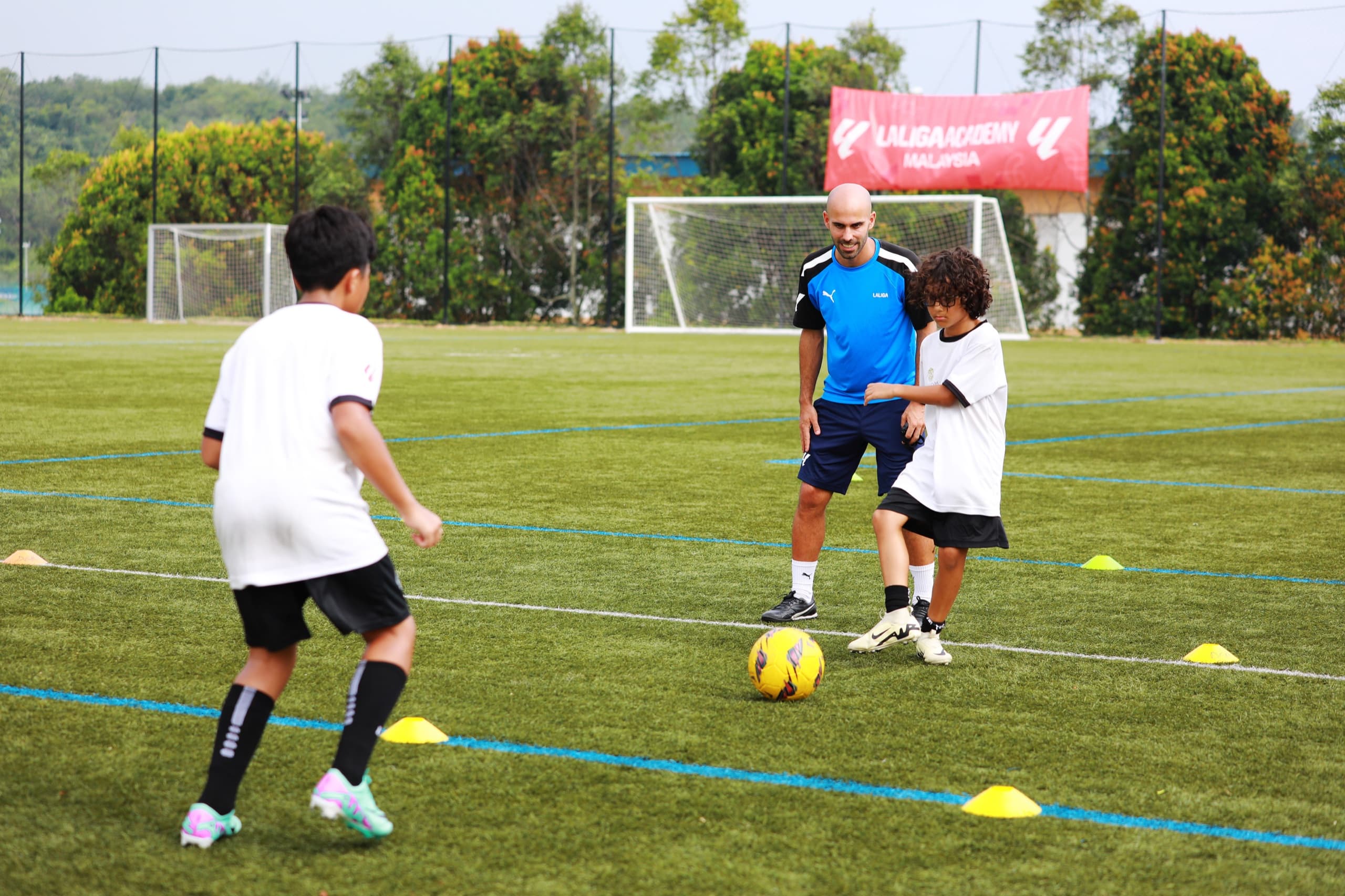 A LALIGA Academy coach running a ball drill with two young players on a pitch at Epsom College Malaysia