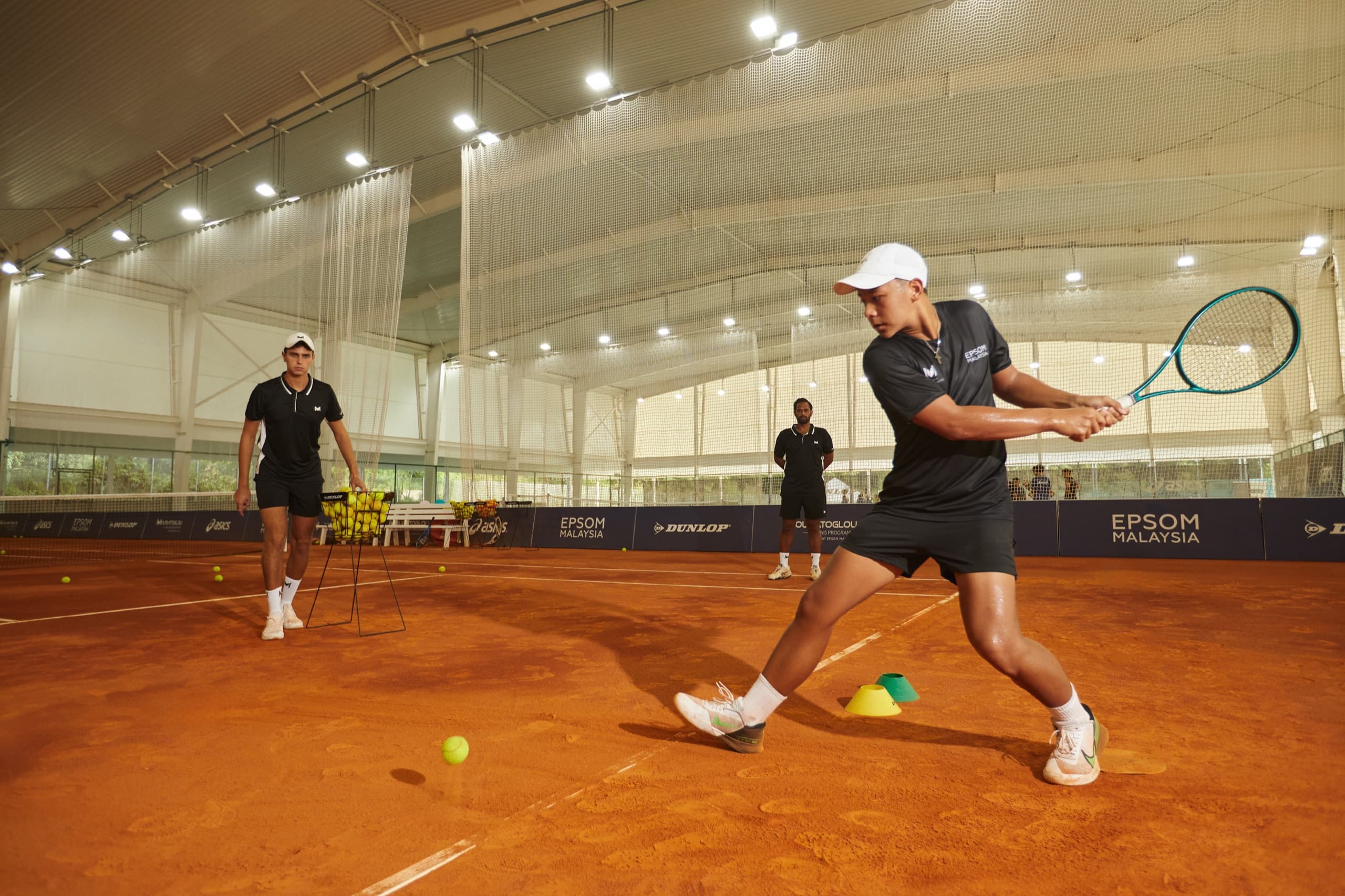 A player hitting a backhand on the indoor clay courts at Epsom College Malaysia